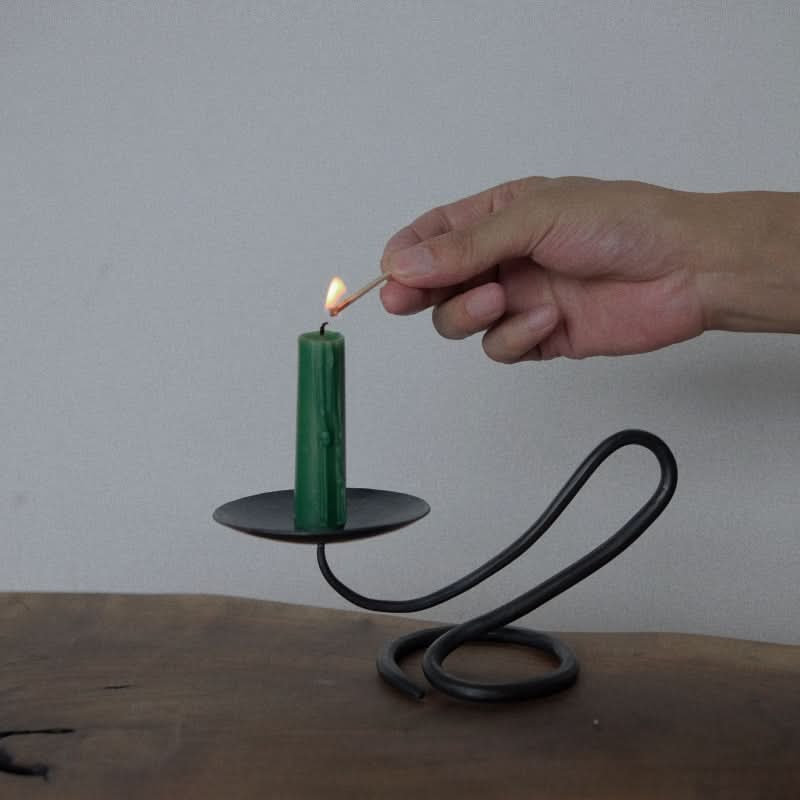 Stylish black candle holder with green candle being lit on wooden surface.